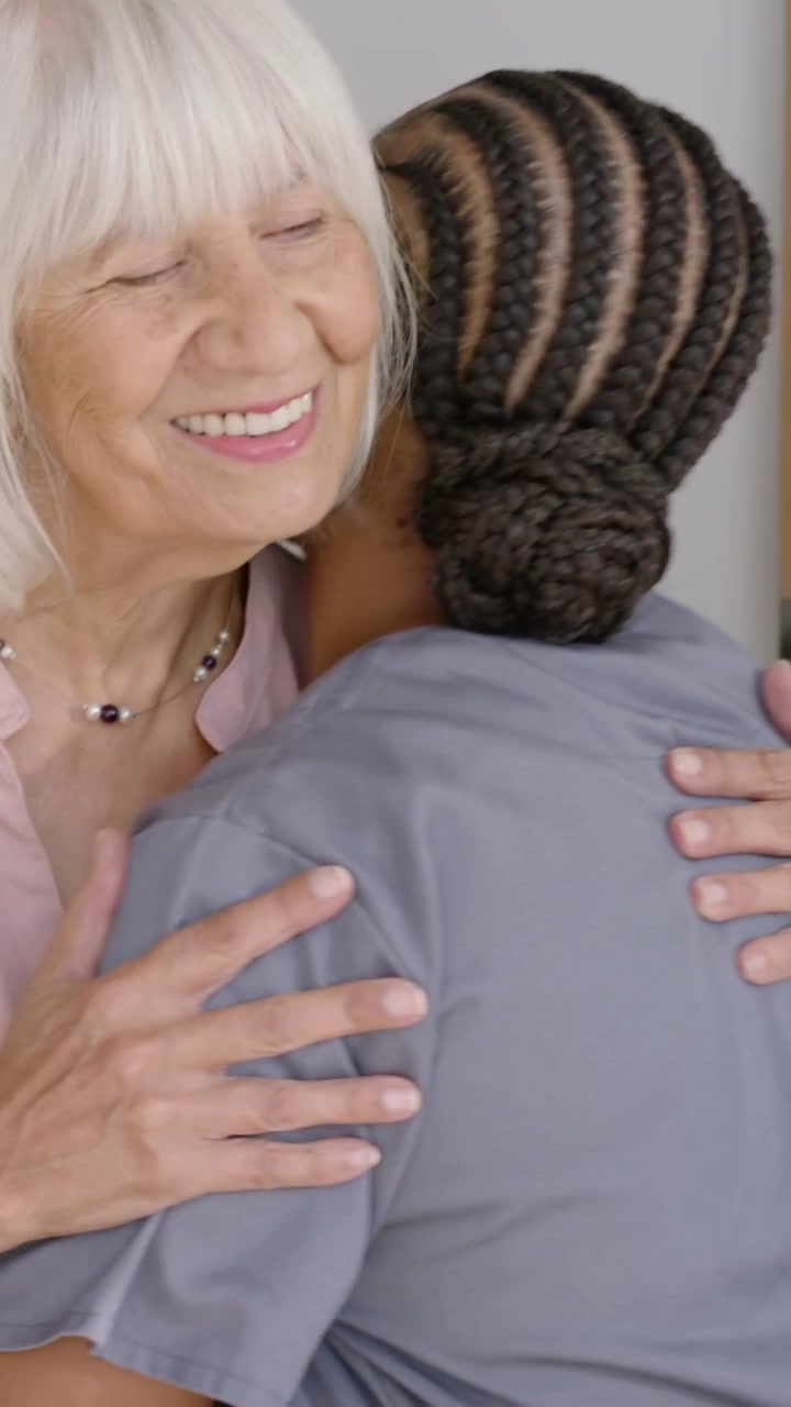 Video verticale: Badante che arriva e abbraccia un anziano alla porta, salutando, in divisa medica, con collana, spazio per il testo