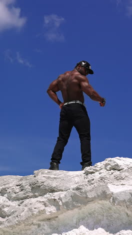 strong athletic man fitness model. low angle view of the guy with naked torso showing six pack abs. clear blue sky on the background. vertical video