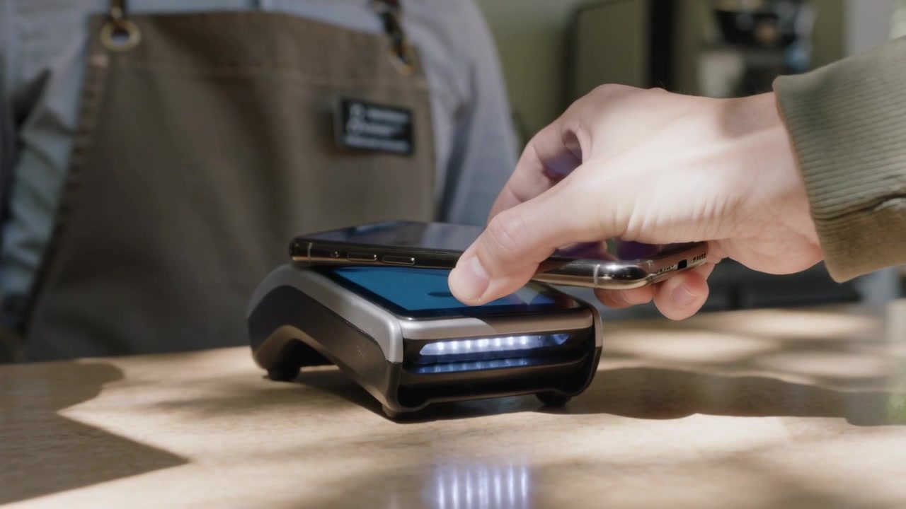 Placing right hand phone over reader at cafe, lighting, paying, aproned staff waiting, copy space