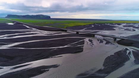 Antenne-Eines-Autos-Entlang-Einer-Straße-Und-Brücke-über-Ein-Großes-Dunkles-Vulkanisches-Hochwassersystem-In-Island-Ice