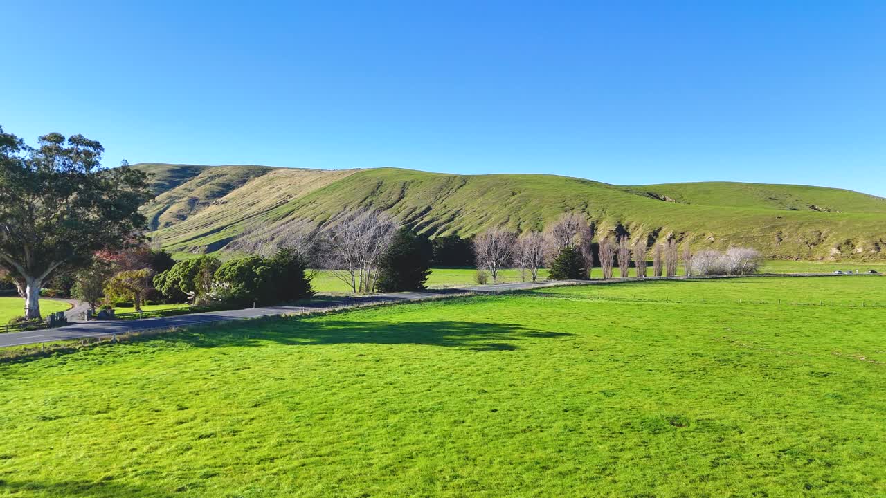 Aerial view of lush green fields and rolling hills under clear blue skies in Akaroa, New Zealand