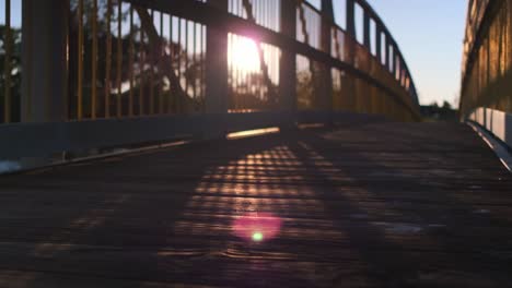 sun shining through the metal rails of a pedestrian bridge over a river during sunset