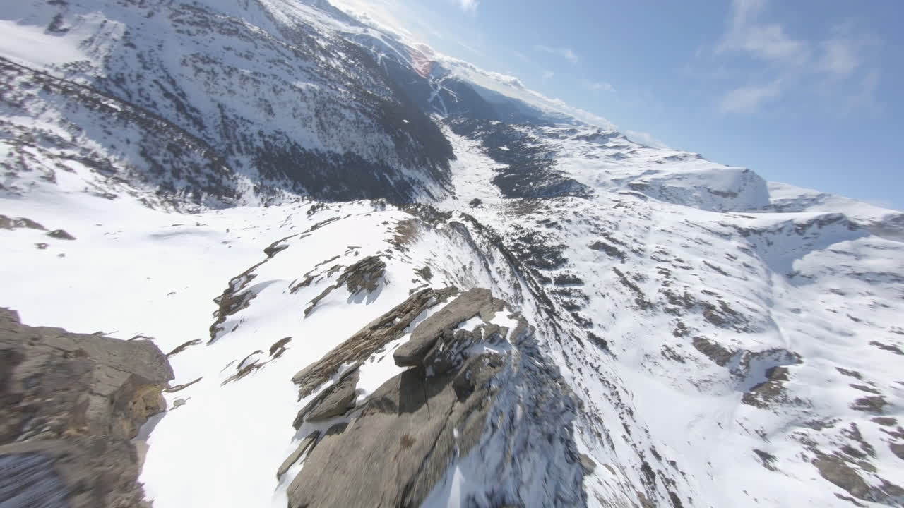 drone acrobático volando sobre montañas rocosas cubiertas de nieve, pirineos