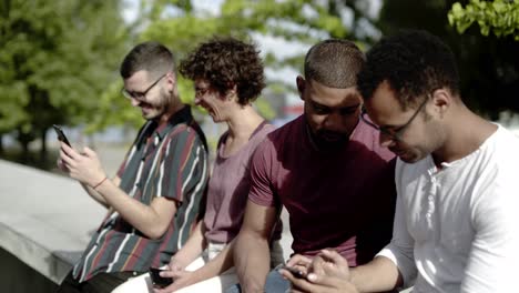 amigos felices sentados en el parque y usando teléfonos inteligentes