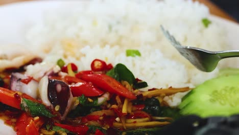 a vibrant plate featuring rice, sliced cucumbers, and a mix of colorful vegetables with a fork.