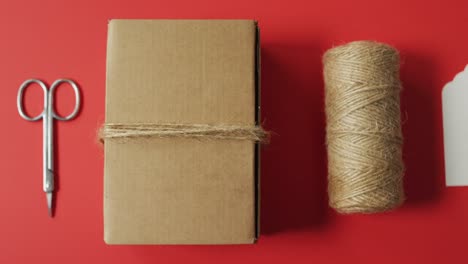 Scissors, box, string and fir tree branch on red background