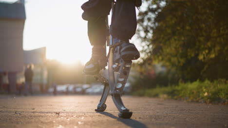 primer plano de la pierna de un hombre usando pilotes de primavera en un área al aire libre suburbana con pantalones oscuros y zapatillas de deporte. el fondo muestra árboles borrosos, edificios y calles. el bajo ángulo de la cámara enfatiza el movimiento