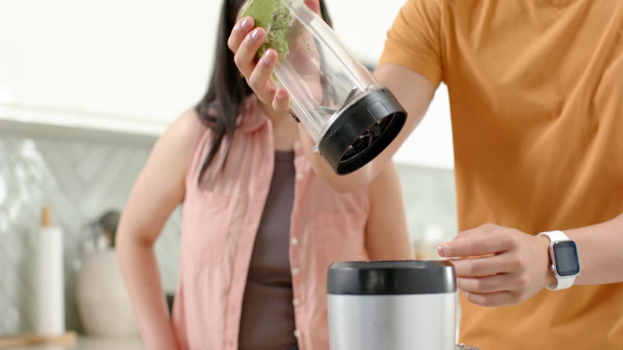 Coppia asiatica che prepara un frullato verde in casa, l'uomo chiude il coperchio e avvia il frullatore per un'alimentazione sana
