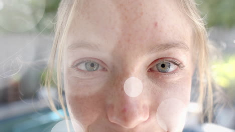 animation of light spots over portrait close up of happy caucasian teenage girl in garden