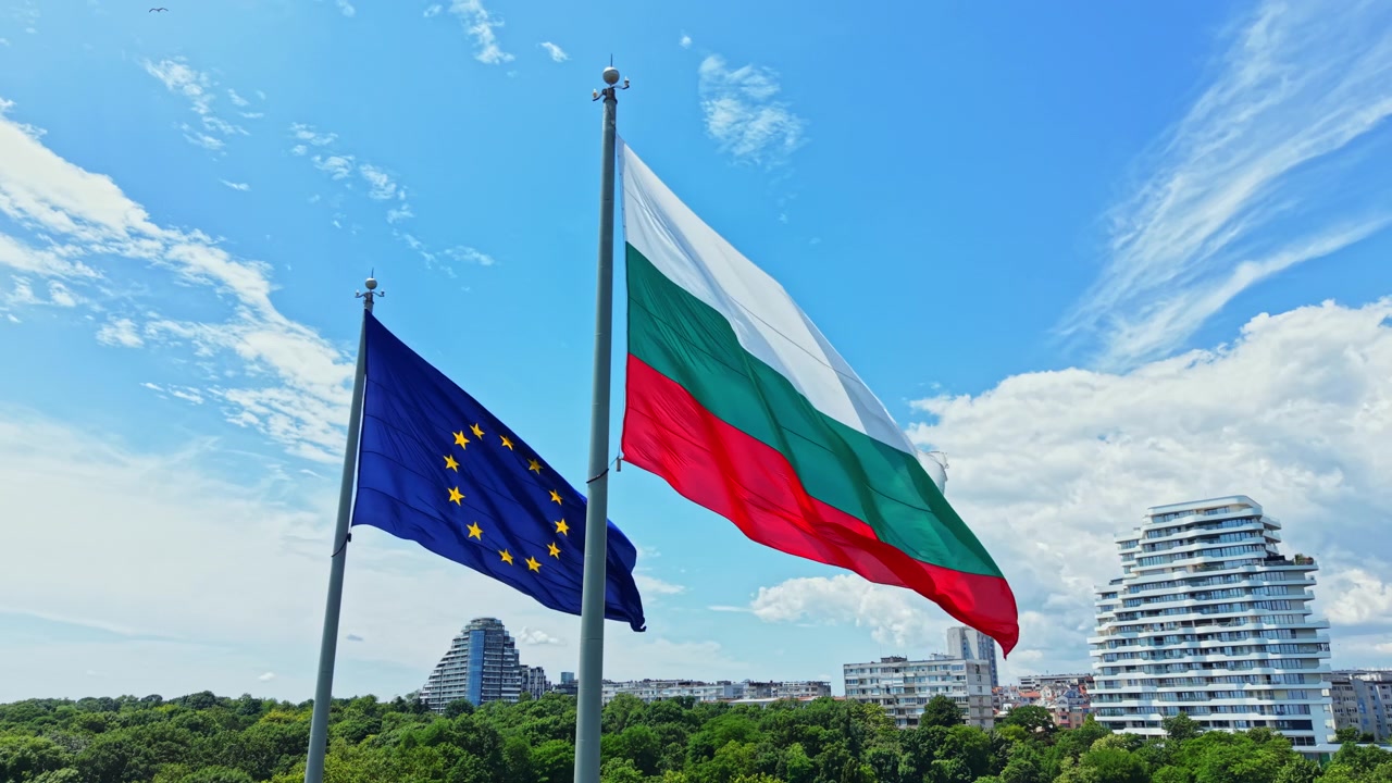 Bandiere della Bulgaria e dell'Unione Europea che sventolano nel cielo vicino a edifici in una città di giorno