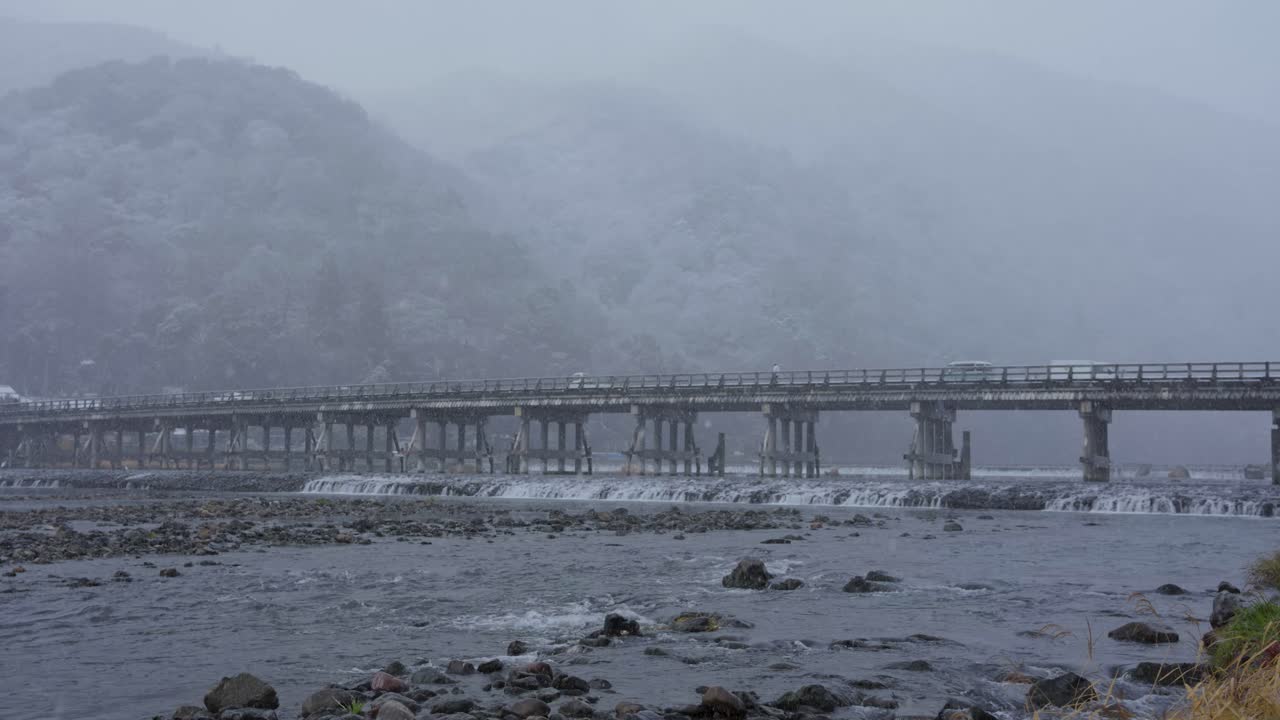 토게츠키오 다리와 카쓰라 강 위에 눈이 내리고, 배경에는 아라시야마가 있습니다.
