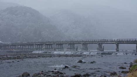 snow fall over togetsu-kyo bridge and katsura river, arashiyama in background