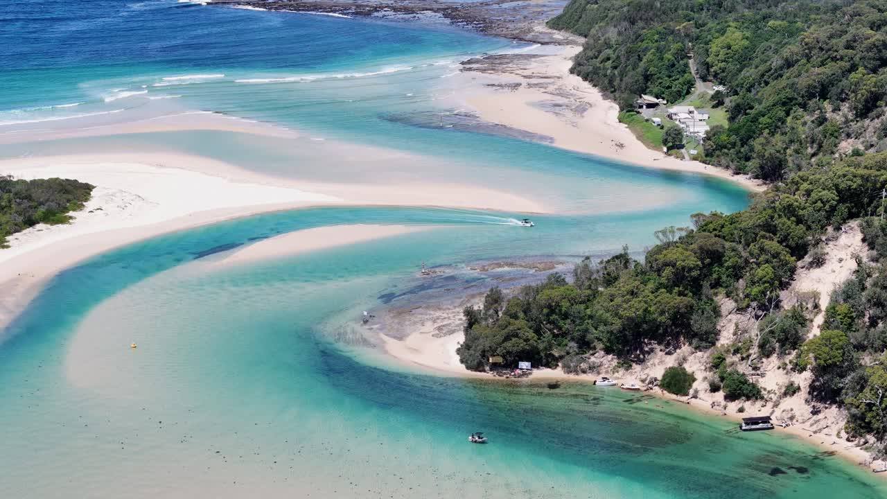 Drone tilt up of winding waterways and sandbanks at Sussex Inlet, NSW, Australia, in bright daylight as boat drives up
