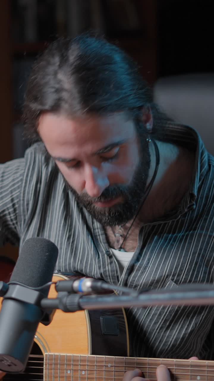 Man with beard playing acoustic guitar and singing into a microphone
