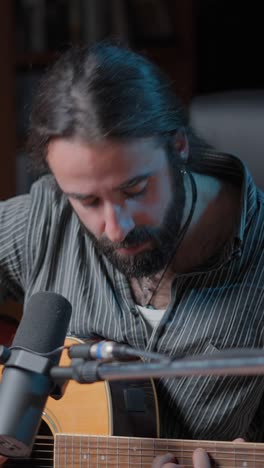 man with beard playing acoustic guitar and singing into a microphone