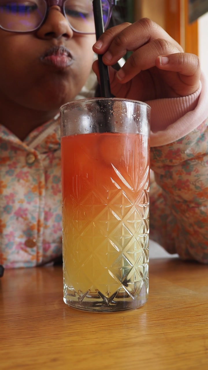Young Girl Drinking a Vibrant Layered Drink with a Straw