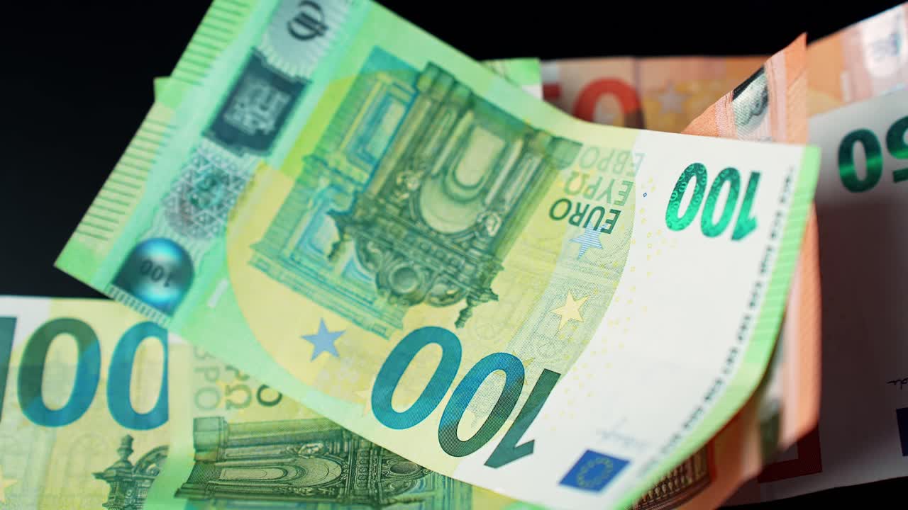 Primo piano di una mano che posiziona una banconota da 100 euro su una pila su sfondo scuro, concetto di pagamento, risparmi e finanza personale