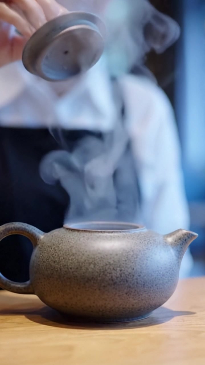 A skilled barista carefully places the lid on a steaming teapot, emphasizing the artistry and precision involved in preparing a perfect brew in a cozy café setting.