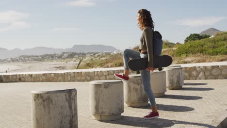 mixed race woman holding skateboard stopping to enjoy the view by the sea