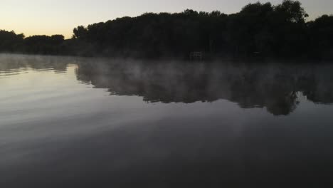 mystical low angle drone flight over foggy tranquil amazon river during colorful sunset in background. silhouette of trees and plants on shore. pan shot. aerial view 4k