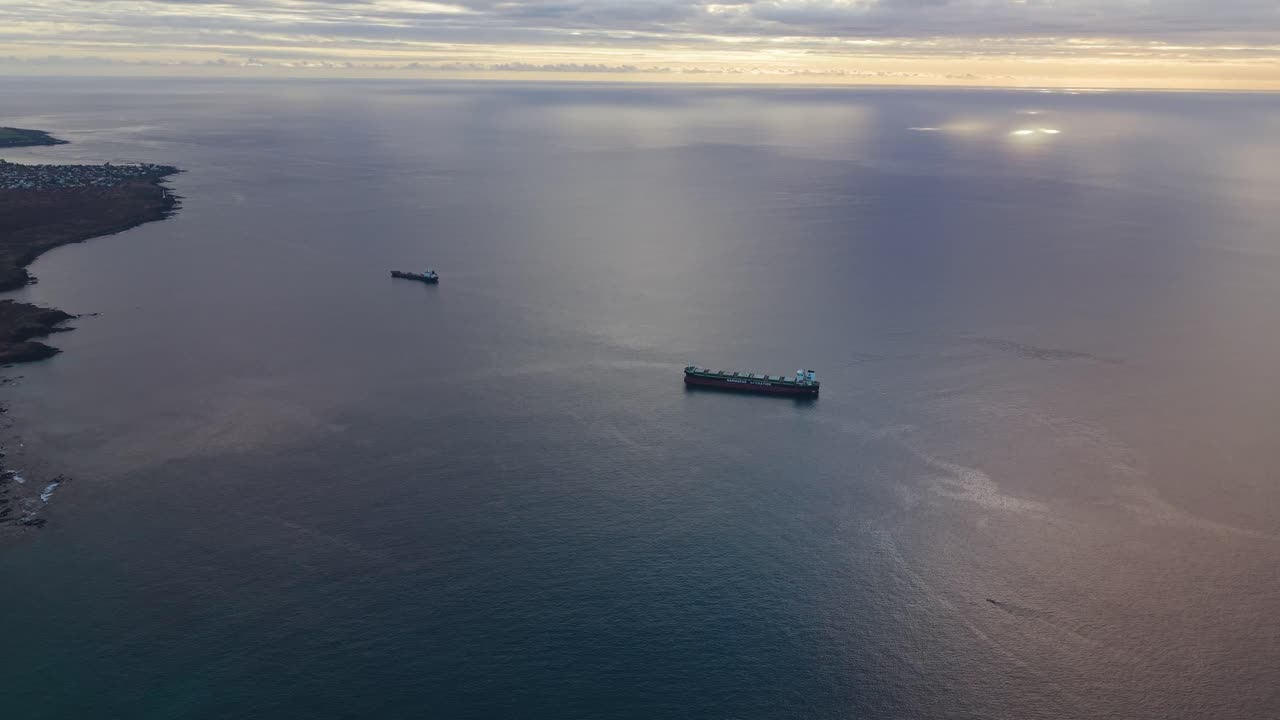 Oil tankers anchored off the Mauritius coastline at sunset, reflecting warm light across the tranquil ocean. A calm maritime scene highlighting trade and coastal energy transport