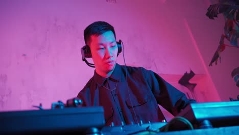 modern dj of asian appearance performs a music track in neon lighting.