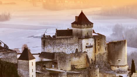 Aerial-view-of-Castelnaud-castle-in-the-morning,-close-up-of-the-architecture-of-this-magnificent-riverside-castle-in-orange-and-blue-light