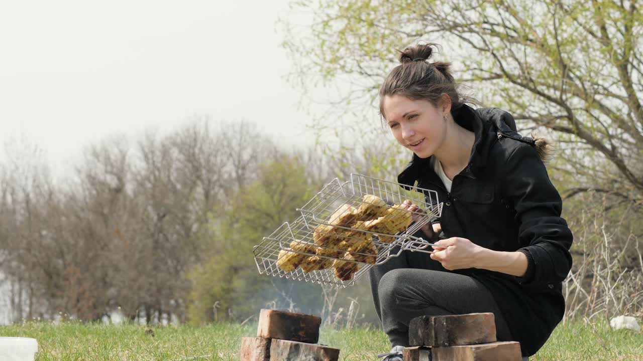 Young woman cooking meat barbecue on fire during picnic on nature