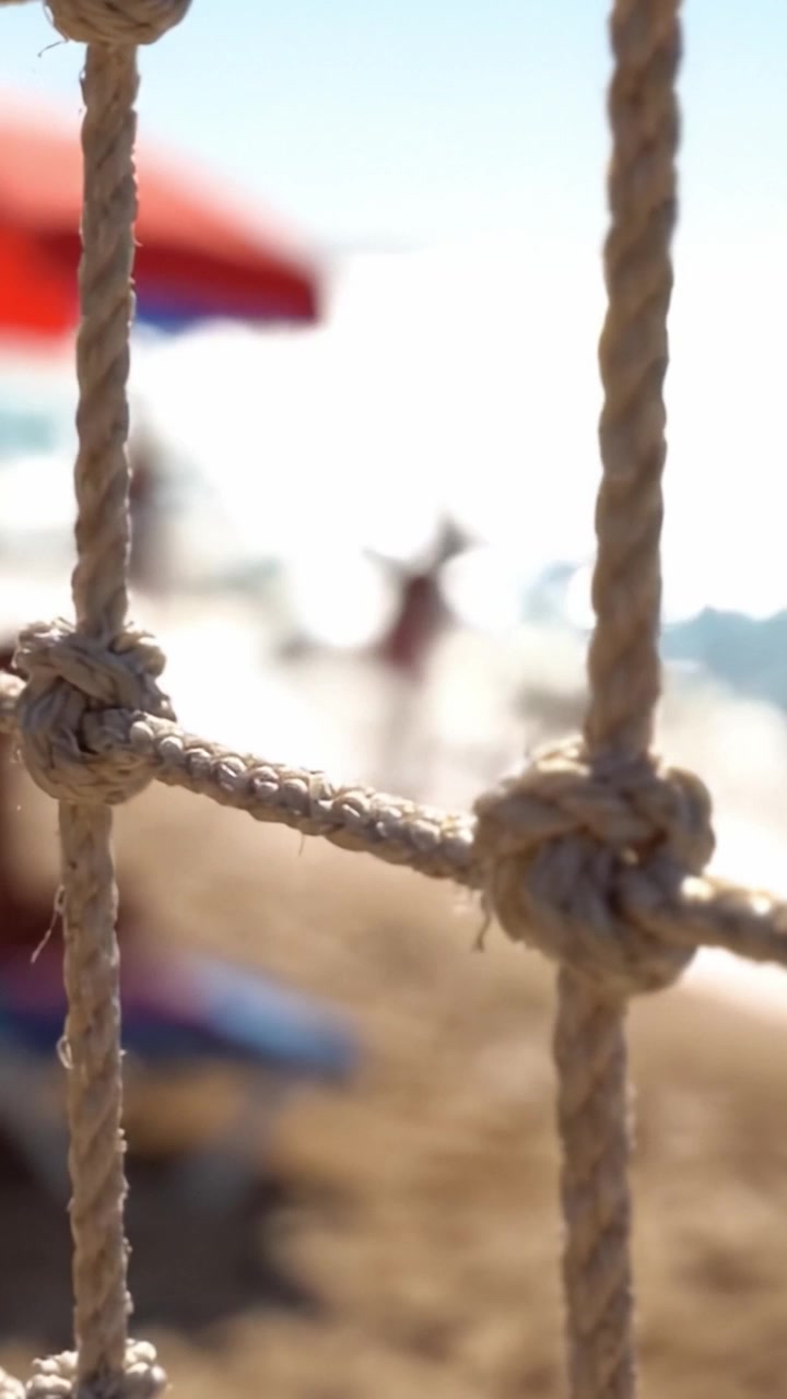 Una serena scena da spiaggia incorniciata da una corda annodata: una vista attraverso una barriera di corda che cattura l'essenza del tempo libero e del relax in riva all'oceano.