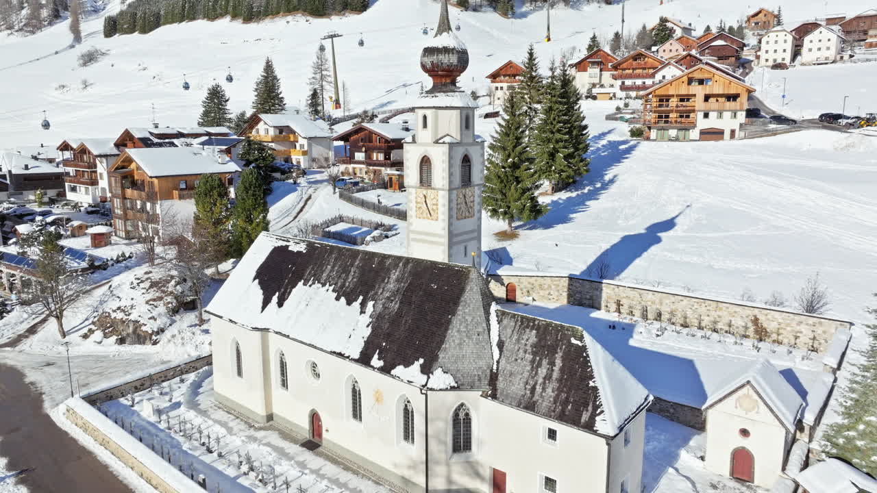 Aerial drone view of the Parrocchia di Colfosco in the Colfosco mountain village covered in snow, in South Tyrol, Dolomites, Northern Italy