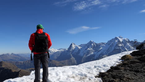 man-with-red-coat-and-green-cap-enjoys-the-wonderful-views-and-mountains-of-Jungfraujoch,-known-as-top-of-Europe