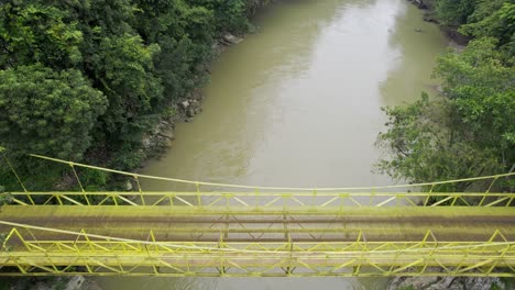 drone aerial footage of yellow bridge over river rio cahabon near semuc champey national park in guatemala surrounded by bright green rainforest trees near chicanutz