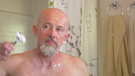 White-man-shaves-side-of-his-head-with-a-razor-in-front-of-a-mirror,-reflection-view