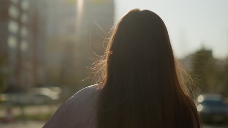 close-up of a girl with long brown hair flowing, wearing a peach jacket, walking through an urban area at sunset. the warm sunlight creates a serene and tranquil atmosphere as she moves forward