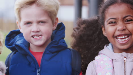 niños de la escuela jóvenes con abrigos de pie fuera de la escuela sonriendo a la cámara, tiro de panorámica de mano