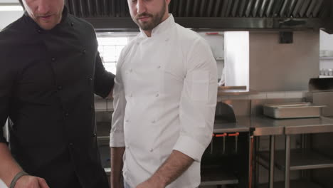 focused caucasian male chef instructing trainee male chef in kitchen, slow motion