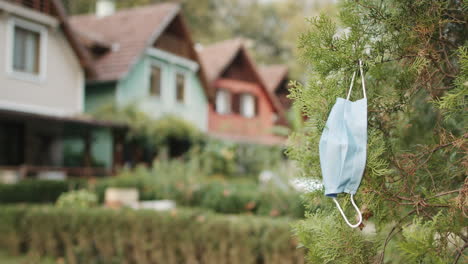 a covid19 protection mask hanging from green tree branch, causing environmental pollution and excess waste in slowmo