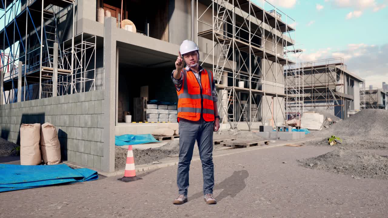Full Body Of Asian Male Engineer With Safety Helmet Disapproving With No Index Finger Sign While Standing At Building & Construction Site in Progress to New House