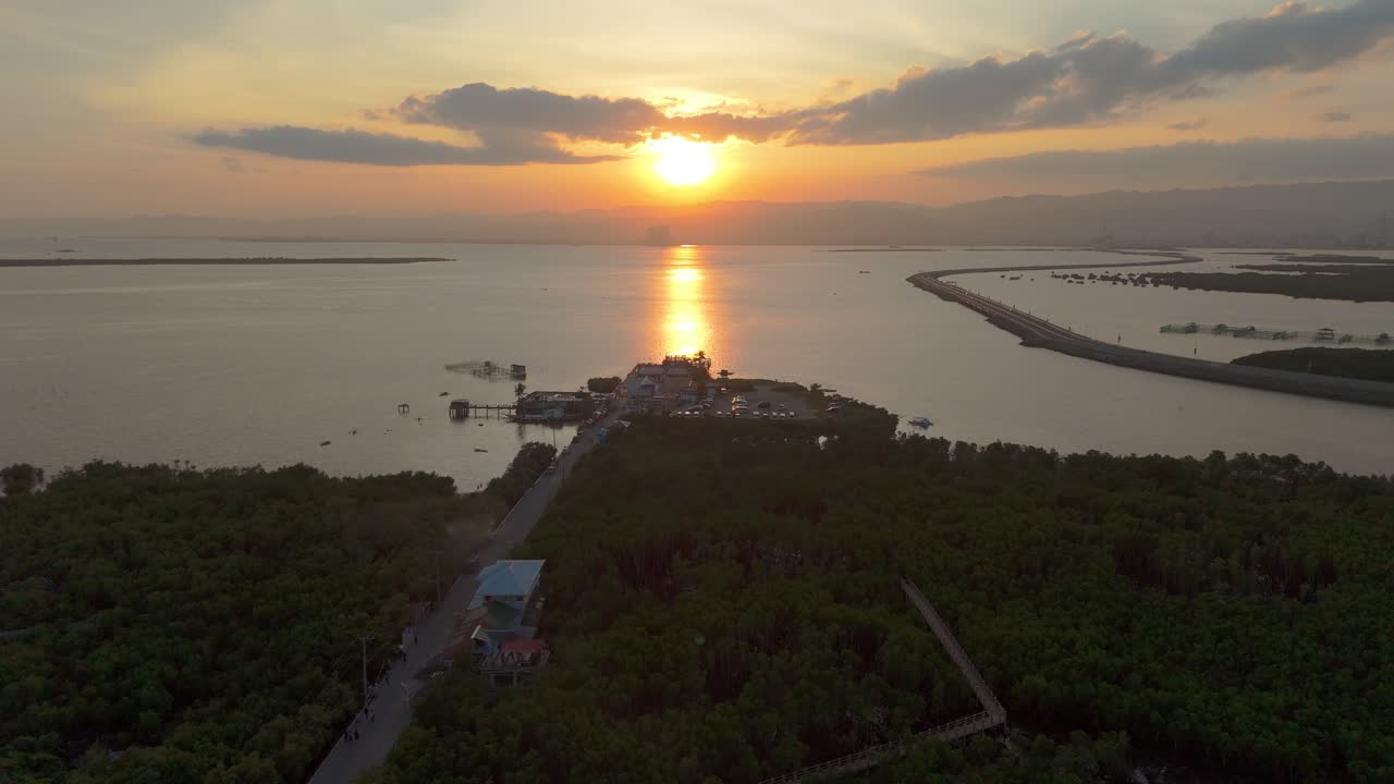 Medium drone shot of sunset over a coastal bay with a long island road, glowing water reflections, and distant skyline in the Philippines. Peaceful and cinematic mood