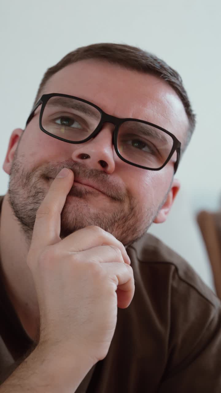 Primer plano vertical de un hombre con gafas apoyando el dedo en su cara mientras piensa, capturando la contemplación, la toma de decisiones y un estado de ánimo tranquilo y reflexivo en un auténtico retrato de estilo de vida.