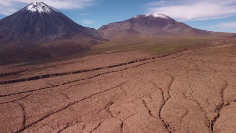 aerial view of snow capped licancabur volcano at the chile–bolivia border. cracked desert ground, volcanic slopes, and dramatic textures of the andean plateau.