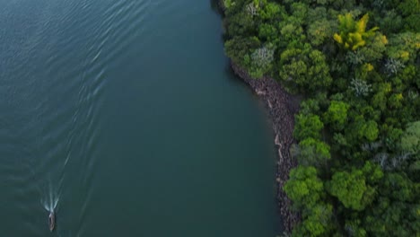 Pan-up-drone-shot-flying-over-the-Paraná-river-at-the-Apipé-island-in-Corrientes,-Argentina-as-two-motorboats-pass-underneath-during-sunset