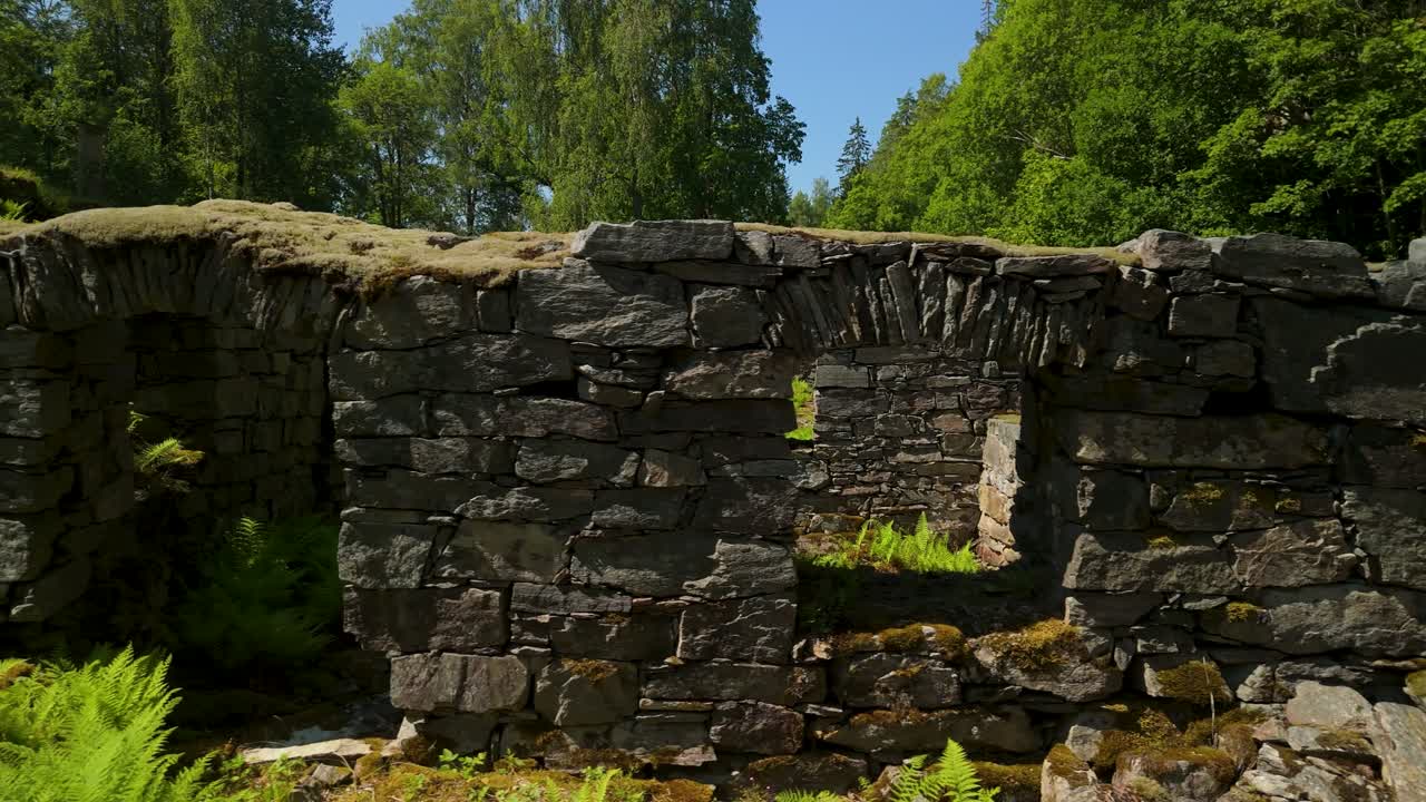 Bäckefors Bruk, Sweden - aerial glide, ancient stone forge ruins, arched doorway, moss-covered walls, ferns, lush summer forest in sunlight