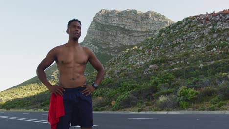 hombre afroamericano de pie y flexionando sus músculos en una carretera costera