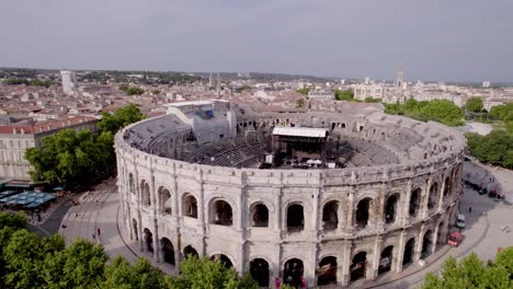 Aerial-view-that-tilts-between-two-trees,-to-reveal-the-arenas-of-Nîmes,-the-Roman-museum