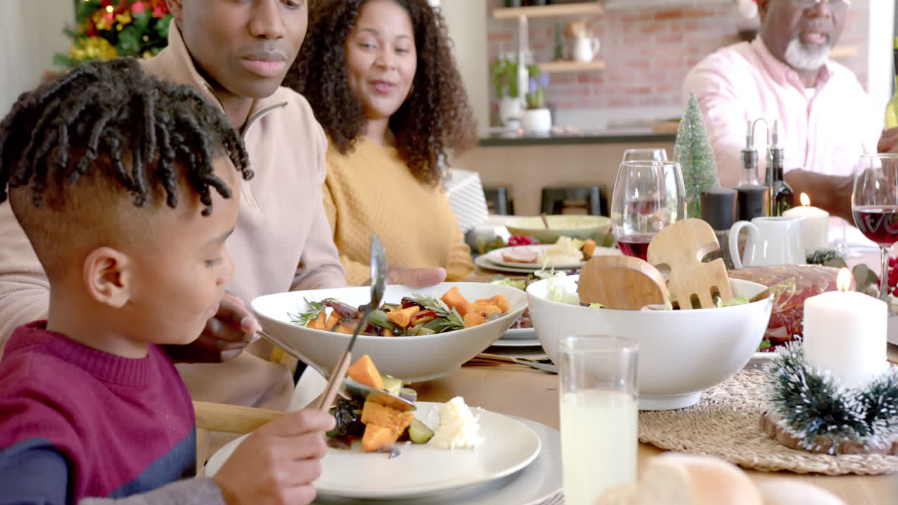 Happy african american father serving son food at family christmas dinner table