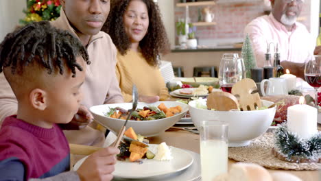 happy african american father serving son food at family christmas dinner table