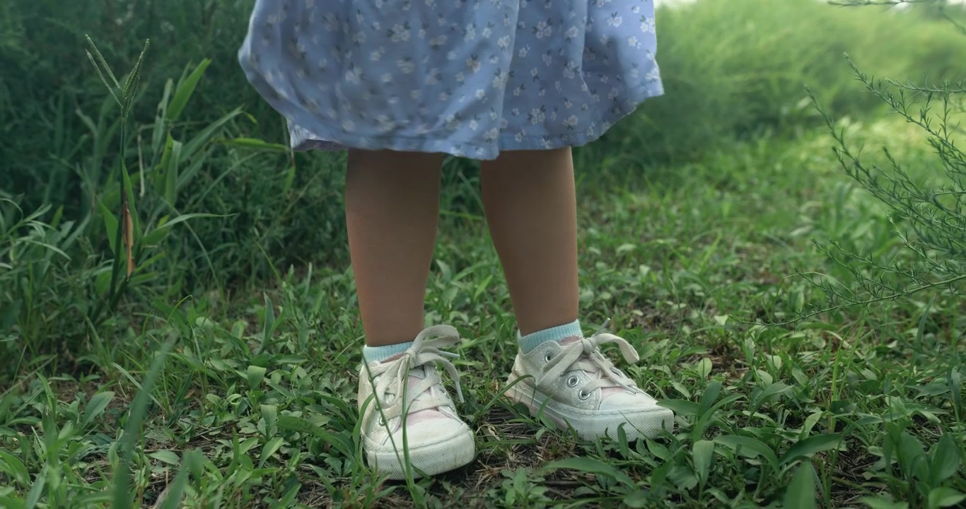 Close-up kaki seorang anak melangkah di atas rumput hijau lembut. Gerakan lembut itu menyoroti momen musim panas yang riang.
