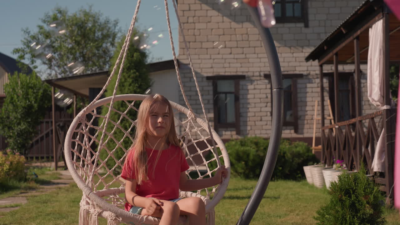 Caucasian Girl On Swing Chair In Sunlit Backyard Garden By Wooden Cottage, Wearing Pink Dress And Barefoot On Grass, Gently Swaying And Smiling In Warm Summer Light, Macrame Hanging Seat, Cozy Porch