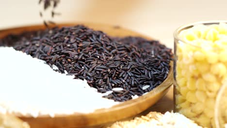 riceberry and white rice in a wooden bowl with corn kernels. dynamic pouring action captured in warm lighting
